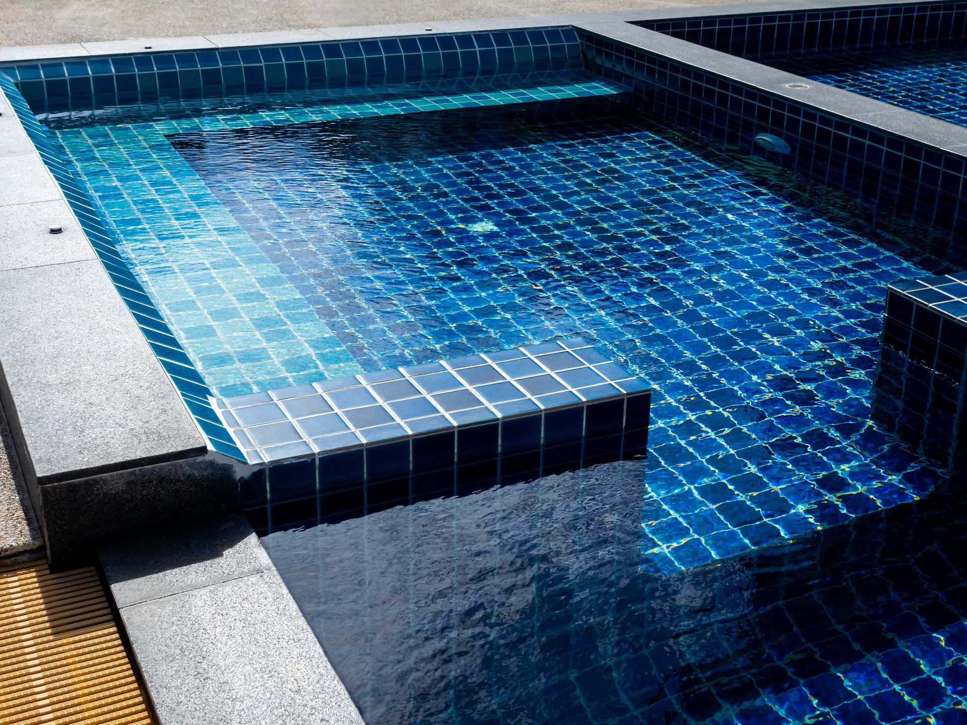 Floating bench seat, sitting zone in swimming pool with clean clear water, nobody. Square shaped pool with blue tiles, no people. Summer background.