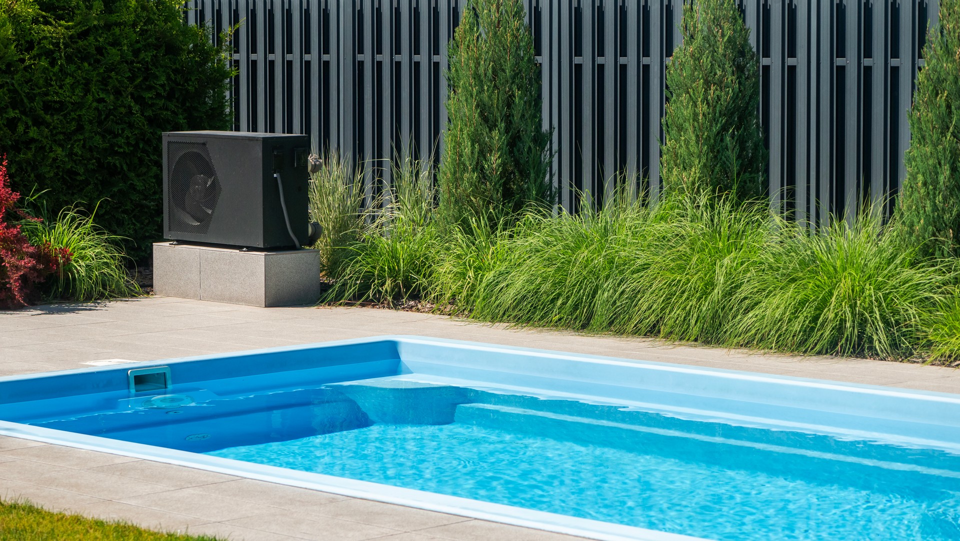 Heat pump unit beside a swimming pool with decorative greenery.